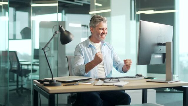 Happy mature bearded Business Man Employee Working on pc computer Celebrates Successful YES Gesture. Working in moderm office Stroke of Luck, Wins Big. Senior worker victory good news financial deal