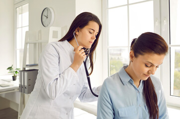 Young female doctor checks woman's breathing and heartbeat at appointment at medical clinic....