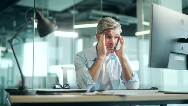 Exhausted, overworked mature office worker sitting in the workplace with a severe headache massaging his head. unhealthy Tired male employee in pain ache sick Stress at work sedentary working computer