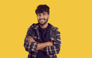 Portrait of handsome attractive positive indian or arabian guy on orange background. Happy young ethnic man in checkered shirt stands with folded arms and smiling friendly at camera. Banner.