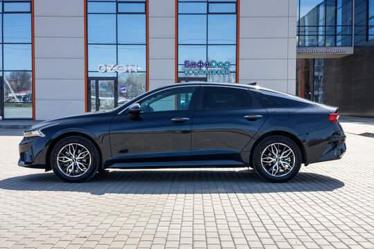 Samara, Russia - 04.16.2022: New KIA K5 in dark blue color.  A car on the background of a business center. The car is parked on an asphalt road. Shooting on a clear, sunny day. Side view of the car