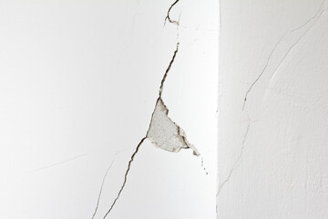 Damaged white wall with a long crack or rip and a piece of plaster missing. Concept of...