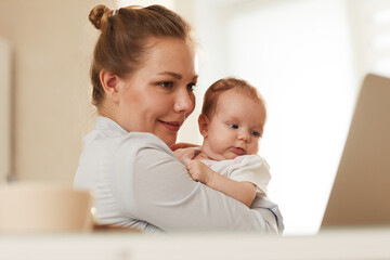 Young smiling mother showing her baby to grandmother who is calling them through Skype