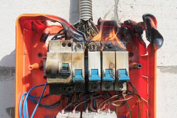 Burning switchboard from overload or short circuit on wall. Circuit breakers on fire and smoke from...