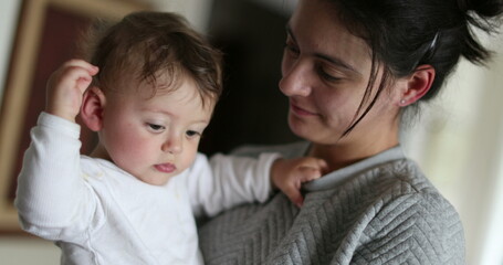 Casual mother holding baby. Mom kisses infant in arms. Real life smile smile and love. Parent kissing son