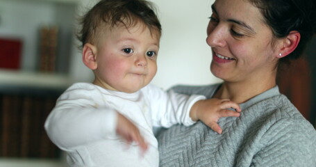 Casual mother holding baby infant in arms smiling and laughing. Real life candid laugh and smile