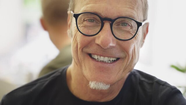 Portrait of a mature happy man or a businessman with black glasses at the restaurant looking at the camera and smiling.