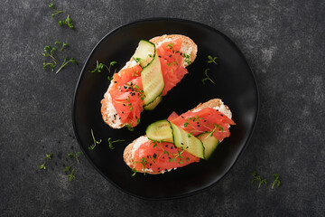 Sandwiches. Salmon toast with cream cheese, cucumber, black sesame and microgreens on black background. Seafood. Healthy food. Photography in low key. Top view.