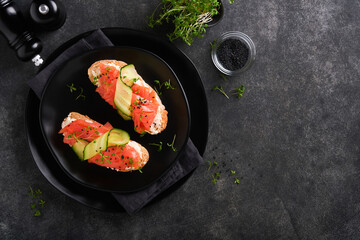 Sandwiches. Salmon toast with cream cheese, cucumber, black sesame and microgreens on black background. Seafood. Healthy food. Photography in low key. Top view.