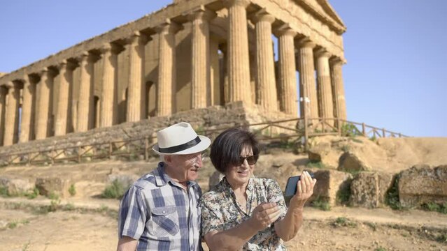 A mature travelers couple takes a selfie in the Valley of the temples, in front of the Temple of Concordia, in Agrigento, an ancient city of Sicily, in Italy.