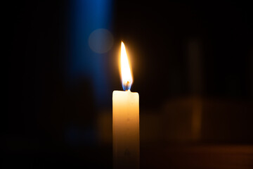 Yellow candle is burning in a dark room. Blue stripe of light, hot fire. A symbol of sorrow,...