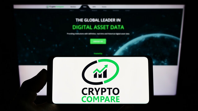 Stuttgart, Germany - 02-26-2022: Person holding smartphone with logo of British financial company CryptoCompare on screen in front of website. Focus on phone display.