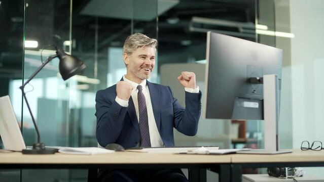Happy mature bearded Business Man Employee Working on pc computer Celebrates Successful YES Gesture. Working in moderm office Stroke of Luck, Wins Big. Senior worker victory good news financial deal