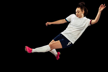 Young caucasian sportive woman, female soccer, football player in motion isolated on dark...