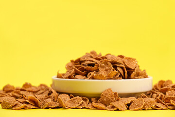 Durum wheat flakes - quick breakfast cereal on a plate on a yellow background, space for text.
