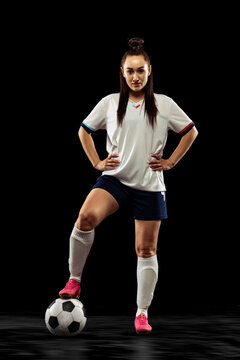 Full-length Portrait Of Sportive Girl, Female Soccer, Football Player Posing Isolated On Black Studio Background. Sport, Action, Motion, Fitness Concept