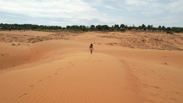 aerial tracking woman walking on top of desert dunes with footsteps in the sand in Mui Ne Vietnam