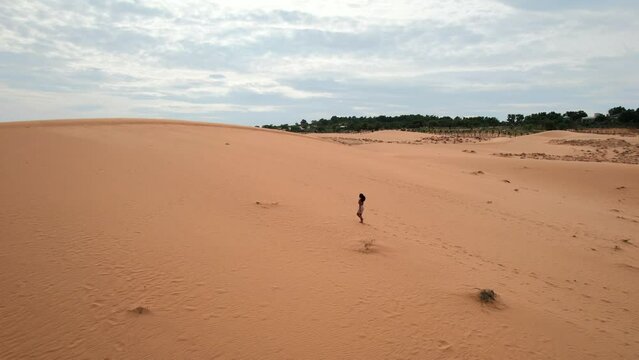 female walking up a red desert sand dune landscape on a cloudy day in Mui Ne Vietnam