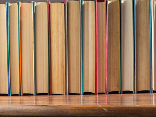 A row  of old hardcover books. Books on a wooden shelf, turned back cover. Books from the Home Library