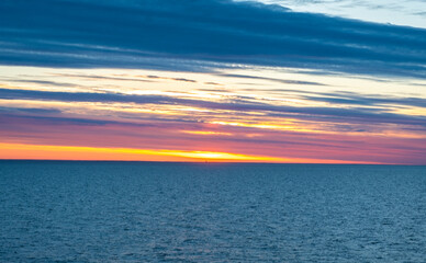 Bright orange sunset over the sea, streaks of sunlight across the sky.