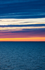 Naklejka premium Bright orange sunset over the sea, streaks of sunlight across the sky. vertical photo