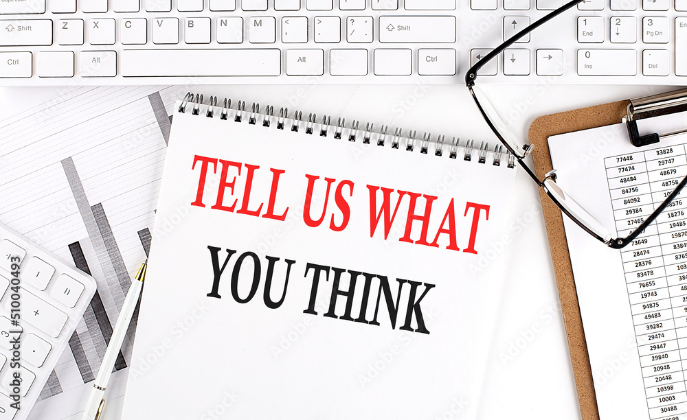 Poster text tell us what you think on office desk table with keyboard, notepad and analysis chart on white 