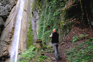 male photographer photographing waterfall giessbach in alpine mountains, fast flowing powerful stream of clear water, splashes scatter, concept of wild nature, natural resources, active sports tourism