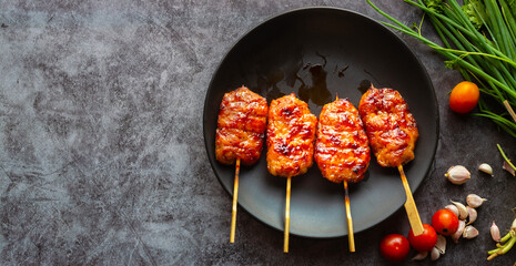 Grill skewered milk pork in a black dish with tomatoes with garlic and spring onion on a gray...
