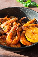 Grilled large shrimps (tiger) cooked in a frying pan with spices, herbs and lemon on a dark background.