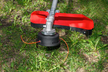 Reel of gas trimmer with fishing line, lawn mower on grass background. Trimmer head