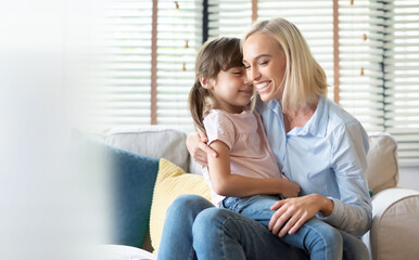 Happy Smiling Mother embracing her lovely daughter sitting on sofa at home together, Mother's day