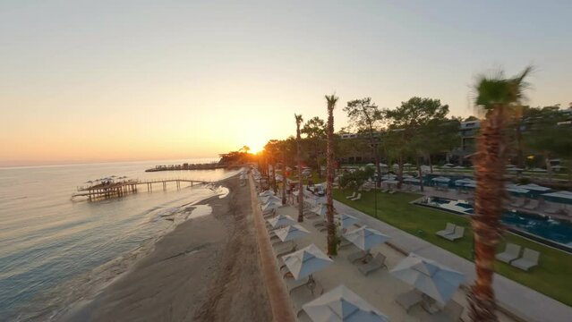 Flight close to Antalya parasol row on resort beach toward glowing sunset; drone