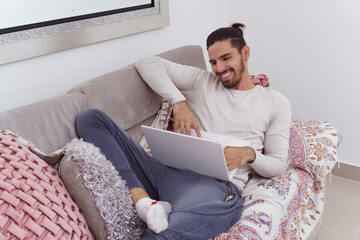 man lying on couch smiling with his laptop
