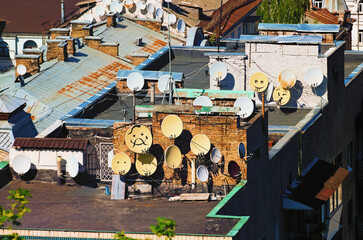 Fototapeta na wymiar Close-up view roofs of residential buildings. A lot of funny decorated satellite antennas on the house's roof. View of the famous Podil neighborhood in Kyiv, Ukraine. Sunny spring day