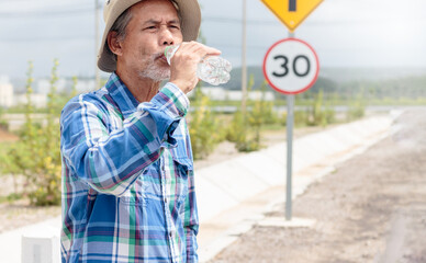 A senior man standing on the street drinking water on a hot day.