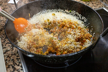 Half height view of a black paella where rice is being cooked with different vegetable ingredients to make a paella