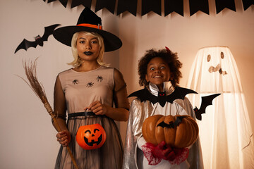 Portrait of African-American mother and son trick-or-treating together on Halloween, they standing against decorated wall