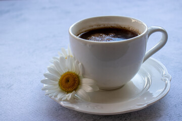 Cup of coffee and white daisy flower on table. Top view of espresso black coffee in white porcelain cup on concrete background with copy space