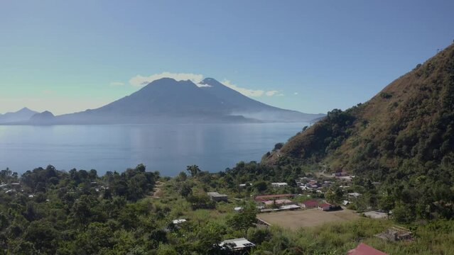 Aerial drone shot flying over sall village on the bank of lake Atitlan, Guatemala, Central America surrounded by beautiful volcanic mountain range at daytime.