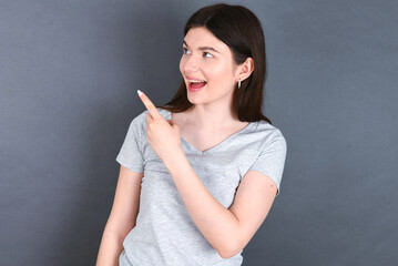  young beautiful Caucasian woman wearing white T-shirt over grey wall glad cheery demonstrating copy space look novelty