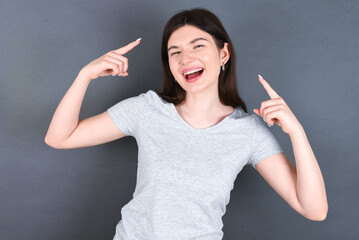 Cheerful  young beautiful Caucasian woman wearing white T-shirt over grey wall demonstrating hairdo
