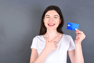 Photo of young happy smiling woman holds and point at bank card earnings profit benefit isolated over gray colour background.