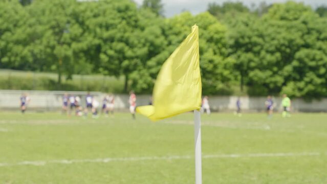 A yellow corner flag waving in the wind on a football field, women soccer teams playing