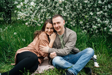 Fototapeta premium young couple in love a girl and a man sit on the grass of a flowering apple tree the aroma of flowers outdoors