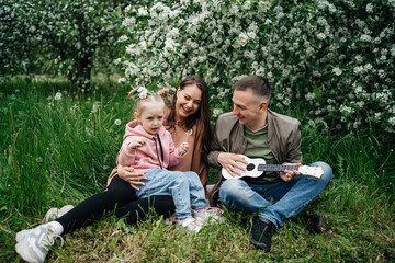 family dad mom baby daughter in the garden blooming apple trees, father playing the ukulele, scent of flowers outdoor nature