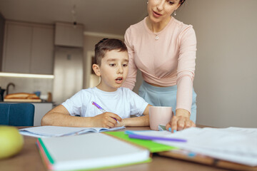 Fototapeta premium Surprised small teen boy looking with big eyes when mother showing mistake in homework.