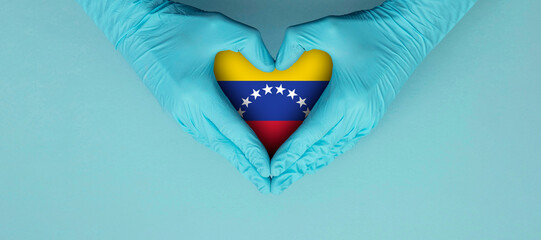 Doctors hands wearing blue surgical gloves making hear shape symbol with venezuela flag