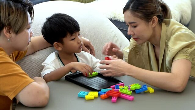 Slow motion shot. Homosexual parents playing with son together in the living room. Asian LGBTQ+ women or gay couple spending time together with children at home.