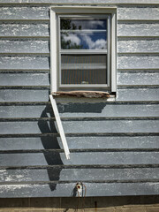 An abstract minimal composition of a piece of fallen trim dangling from a window with a rotted sill...