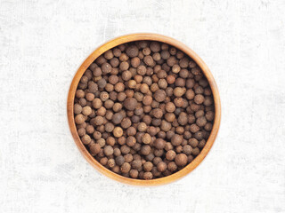Spice Allspice (Jamaica pepper, Pimento) in wooden bowl on white concrete background. Macro. Flat lay. Healthy eating concept